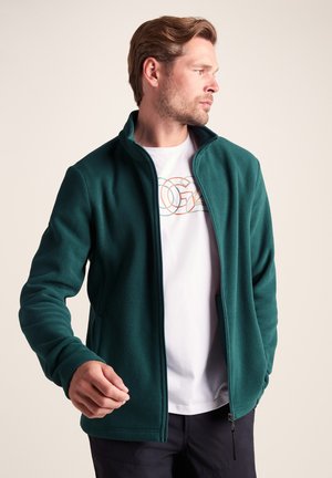 Teal fleece jacket with a high collar, side pockets, and a full zipper. Worn over a white t-shirt with a colorful logo. Smooth texture.