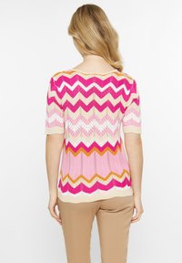 Top de punto de manga corta con un patrón de chevrón en tonos rosa, crema y naranja. Textura suave con cuello redondo y dobladillo festoneado.