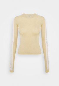 Pull ajusté beige à manches longues avec un léger scintillement et des rayures blanches portant un texte courant le long des deux manches.