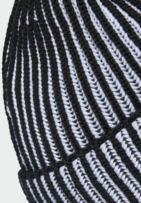 Primer plano de un gorro de punto negro y blanco con rayas acanaladas verticales y ala doblada.