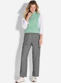 Groene textuurloze mouwloze trui gecombineerd met grijze, gewatteerde cargobroek met zijzakken. Het model draagt lichte sneakers.