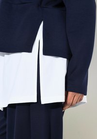 Camiseta de manga larga navy con una capa blanca debajo, con aberturas laterales en el dobladillo y textura de tela suave.