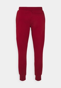 Röda tapered sweatpants med elastisk midja, uppvikta anklar och ett litet bakfack på en vit bakgrund.