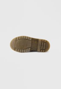 Semelle de chaussure en caoutchouc marron avec une surface texturée, présentant des rainures horizontales et verticales pour une meilleure adhérence et un design de talon arrondi.