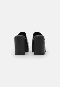 Svart plattformssandaler med overdel i glatt skinn og tykke rektangulære hæler. Minimalistisk design uten synlig maskinvare eller mønstre.