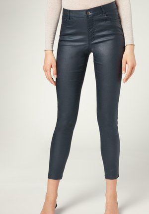 Jeans ajustados de tiro alto de color azul oscuro, fabricados en material elástico. Textura suave, bolsillos delanteros y cierre de un solo botón en la cintura.
