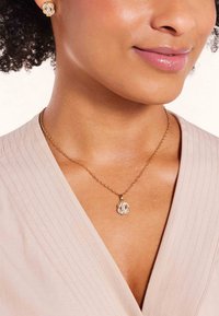 Gouden ketting met een delicate schakel en een hanger met verstrengelde lijnen, geaccentueerd met kleine heldere stenen. Bijpassende gouden studs.