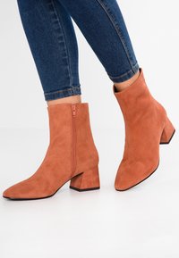 Bruine suède enkellaarsjes met een spitse neus en een blokhak. Kleurige rits aan de zijkant. Gecombineerd met donkerblauwe skinny jeans.