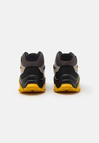 Svarte og gule joggesko med en teksturert mesh-overdel, polstret krage og gummisåle, og med vinklede designelementer og merket detaljer.