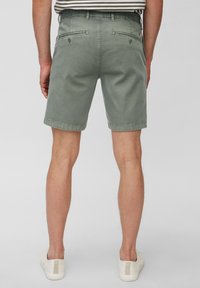 Chino shorts en coton vert avec une coupe décontractée, dotés de deux poches arrière et d'un ourlet roulé, portés avec des chaussures blanches à enfiler.