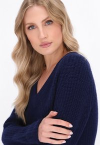 Granatowy sweter dzianinowy z dekoltem w serek, prążkowaną teksturą i długimi rękawami. Posiada luźny krój oraz delikatne detale w st stitching.