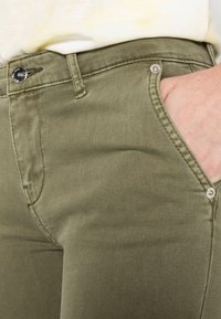 Olivgrön bomullsblandning byxor med en slät textur, framfickor, metallknappstängning och kontrasterande sömnadsdetaljer.