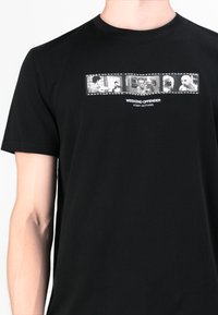 Sort bomulds t-shirt med et rektangulært grafisk design med sort-hvide billeder og teksten "WEEKEND OFFENDER ADMIT NOTHING" nedenfor.
