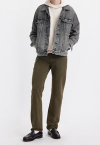 Chaqueta de mezclilla gris sobre una sudadera con capucha en crema, combinada con pantalones verde oliva y mocasines negros. Tejido texturizado con un ajuste relajado.