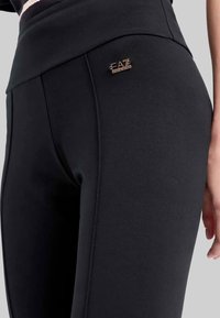 Zwarte sportlegging met een gladde textuur, met een metalen accent met merknaam en een brede tailleband voor comfort. Op maat gemaakte design met naden.
