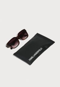Velike sončne očale iz želvje školjke s temnimi lečami poleg črne mehke torbice z belim logotipom "KARL LAGERFELD".