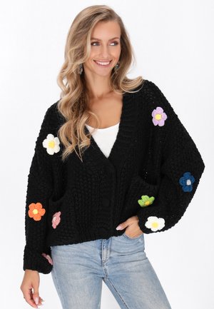 Schwarze Strickjacke mit großen Blumenapplikationen in Orange, Pink, Lila, Weiß, Grün und Blau. Mit V-Ausschnitt und Knopfverschluss.