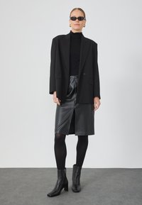 Μαύρη υπερμεγέθη σακάκι, εφαρμοστό μαύρο ψηλό λαιμό, μαύρη δερμάτινη φούστα με μπροστινό σκίσιμο, μαύρες καλσόν και μπότες αστράγαλου. Γυαλιά ηλίου ολοκληρώνουν την εμφάνιση.