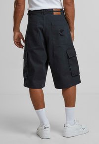 Black cargo shorts with multiple side pockets and contrasting stitching, featuring a logo patch at the back waistband.