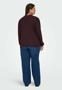 Haut long rouge foncé avec des épaules froncées, associé à un jean bleu ample. Le tissu semble texturé, avec une coupe décontractée.