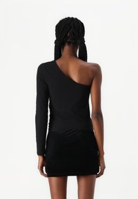 Zwarte top met lange mouwen en een asymmetrisch ontwerp; gladde textuur, slim fit en gecombineerd met een zwarte rok met een fluweelachtige afwerking.