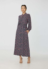 Robe longue à fleurs avec un fond bleu foncé, ornée de motifs roses, un col à revers, des manches longues, une ceinture et des poches latérales.