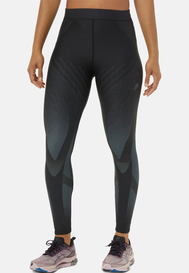 Leggings noirs taille haute avec des motifs géométriques gris, offrant une texture lisse et un ajustement serré. Associés à des chaussures de course violettes claires.