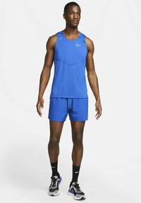 Blaues Nike Sporttanktop mit Mesh-Struktur und reflektierenden Akzenten, kombiniert mit passenden blauen Shorts und schwarzen Socken. Rundhalsausschnitt, schmaler Schnitt.