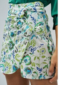 Falda blanca con patrones florales en azul y verde, con un diseño anudado en la cintura y una tela texturizada.