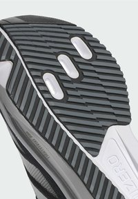 Čierna a šedá športová obuv má podrážku s textúrovaným gumovým vzorom, bielymi akcentmi a ventilačnými otvormi v strede.
