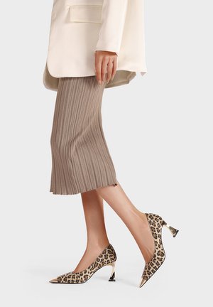 Scarpe con tacco alto in stampa leopardata con punta affusolata e dettagli metallici, indossate con una gonna plissettata beige e un blazer crema.