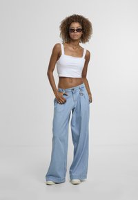 Light blue wide-leg jeans with a ring detail at the waist, paired with a white cropped tank top. Model wears dark sunglasses.