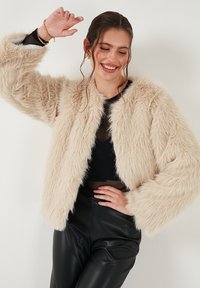 Nepbont jasje in een zachte beige kleur, met een cropped ontwerp, ronde halslijn en lange mouwen met een zachte, fluffy textuur.