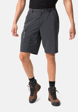 Mann trägt schwarze Outdoor-Shorts mit einer Reißverschlusstasche an der Seite sowie braune Wanderschuhe mit schwarzen Schnürsenkeln und Socken.