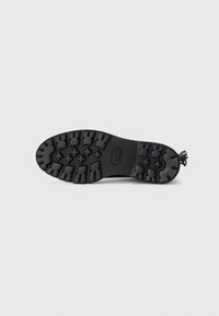 Semelle de chaussure en caoutchouc noir avec des motifs de semelle profonds pour une adhérence, surface lisse et bord de talon arrondi pour le confort et la stabilité.