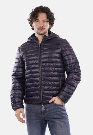 Giacca puffer blu navy con design trapuntato, cappuccio, zip frontale e polsini elasticizzati. Indossata sopra una maglietta grigia e jeans blu.
