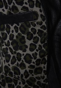 Černá kožená bunda s vnitřním podšívkou s leopardím vzorem v tmavě zelené a černé barvě na světle šedém pozadí. Výrazný detail náprsní kapsy.