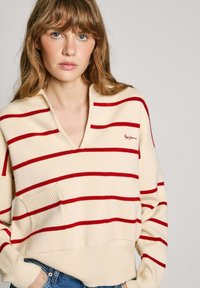 Pullover crema con strisce orizzontali rosse, scollatura a V, tasca frontale, bordo e polsini a coste, realizzato in un morbido materiale a maglia.