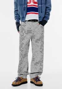 Pantaloni con motivo pixelato grigio realizzati in tessuto con una vestibilità ampia. Abbinati a scarpe marrone con texture e lacci blu, dotati di tasche frontali.