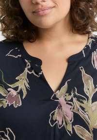 Haut floral marine avec un décolleté en V, orné de motifs floraux roses et verts, en tissu doux et légèrement texturé pour un intérêt visuel.