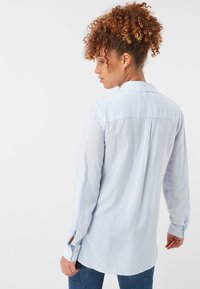 Modrá a bílá pruhovaná košile s dlouhým rukávem, volnější střih, knoflíkové detaily na rukávech a design vzadu s yoke. Bavlněný materiál.
