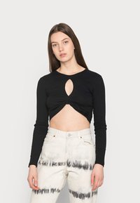 Top cropped preto de mangas longas com um corte em forma de olho-chave na frente, combinado com calças de cintura alta em tie-dye nas cores branca e cinza.
