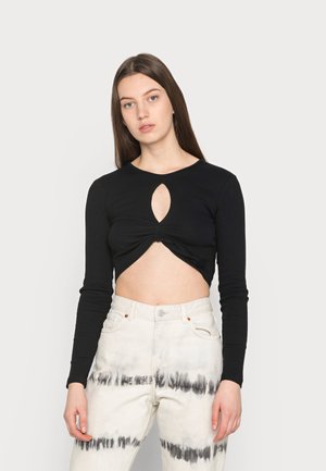 Top cropped preto de mangas longas com um corte em forma de olho-chave na frente, combinado com calças de cintura alta em tie-dye nas cores branca e cinza.