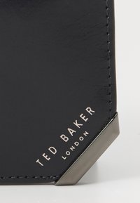 Black leather wallet with glossy finish, featuring silver hardware, angled corners, and embossed "TED BAKER LONDON" logo.