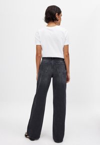 Wide-leg black jeans made of denim, featuring back pockets, a high waist, and a faded finish. Paired with a plain white t-shirt.