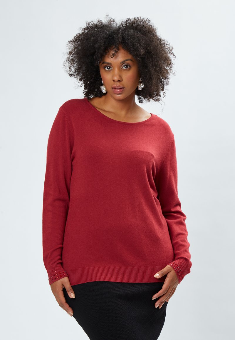 Pullover rosso con scollo a barca, maniche lunghe, orlo a coste e polsini decorati con piccole perline. Texture liscia.