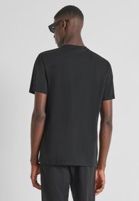 Camiseta negra de manga corta con cuello redondo y dobladillo recto. Confeccionada en una tela suave con una textura sutil; detalle del logo en la parte posterior.