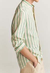 Leichtes Leinenhemd mit vertikalen grünen Streifen auf beigem Hintergrund, mit Stehkragen und Knopfverschluss. Hochgekrempelte Ärmel.