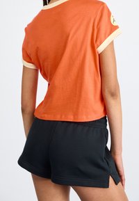 Oranje T-shirt met korte mouwen en crèmekleurige kraag- en boordranden, gecombineerd met zwarte katoenen shorts met een elastische tailleband en zijsplitten.