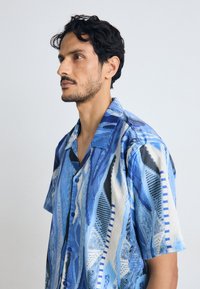Short-sleeve shirt featuring a blue abstract pattern, button front, and a relaxed fit; made from a lightweight fabric.